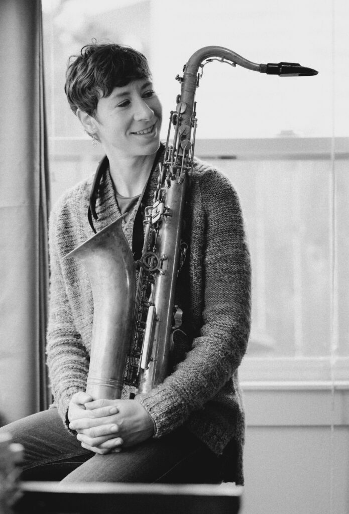 Kristen holding a tenor saxophone and smiling.